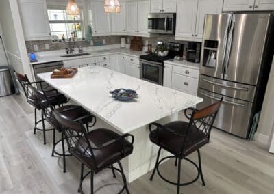 Modern white kitchen with quartz island and bar stools.