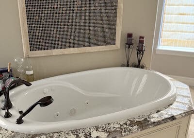 Bathroom tub surrounded by dark natural stone countertop to contrast the white jacuzzi bathtub